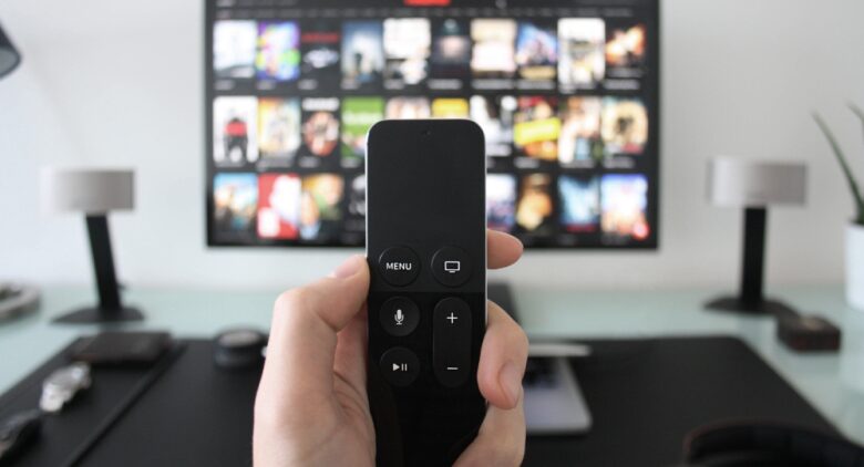 テレビ画面の前でリモコンを持っている手